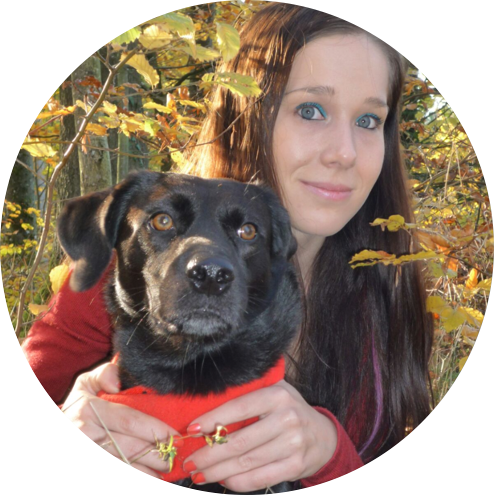 Frau mit braunen Haaren und schwarzem Hund in Herbstlandschaft