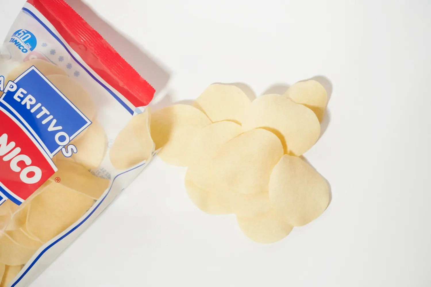 Patatas fritas en forma de rodajas delgadas, de color amarillo pálido, saliendo de un paquete de papas Pringles en una superficie blanca.