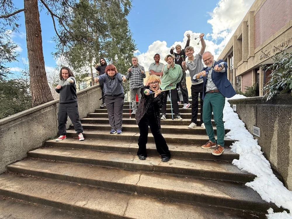 Photo of SOU Percussion Ensemble members on the steps of the SOU Music Building. They are posing in a humorous fashion - pointing their mallets at the camera, goofing around, etc.