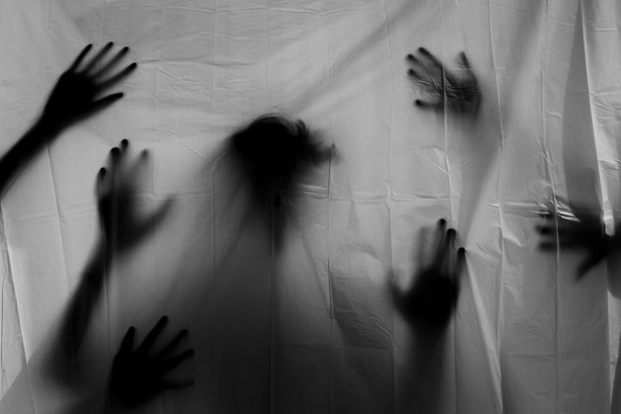 A white curtain hangs with eerie silhouettes of hands and heads behind it.