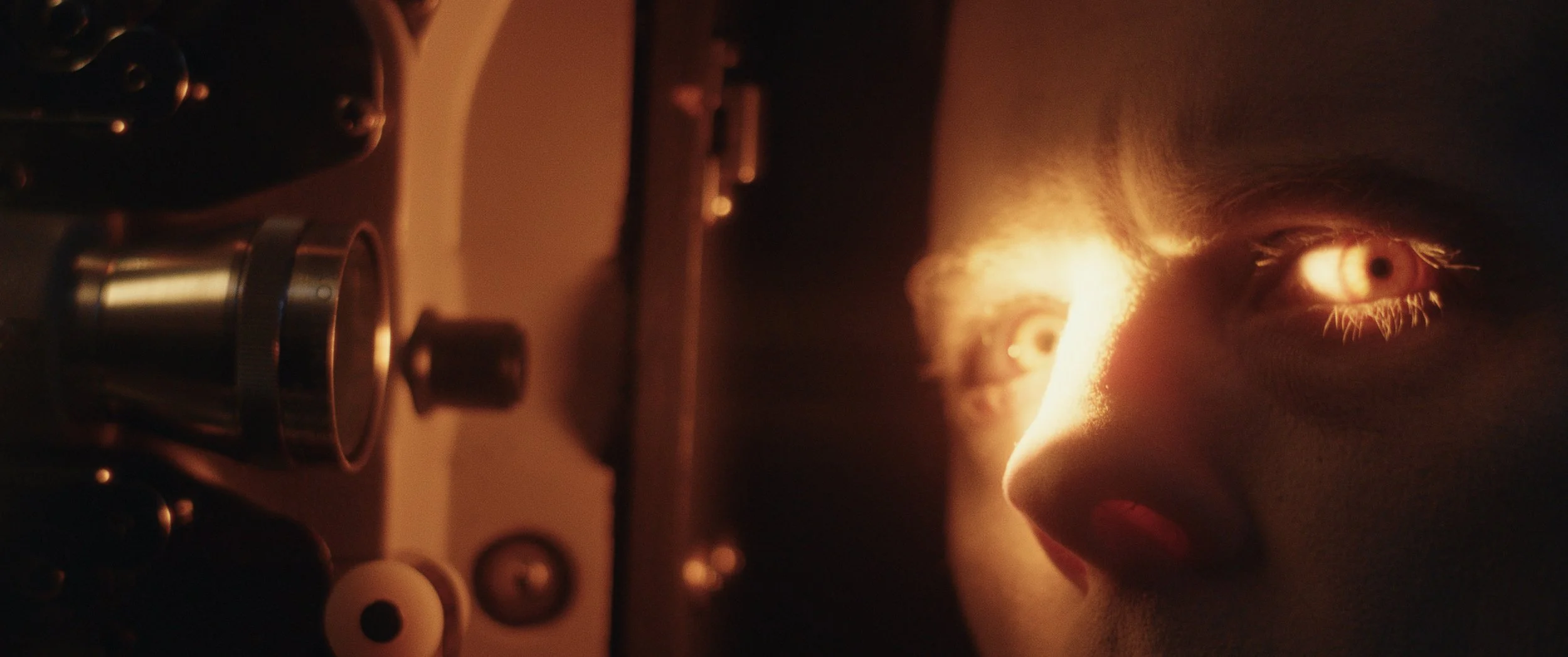 Extreme close-up of a man staring toward the camera, his eyes lit by the light of a projector lens.