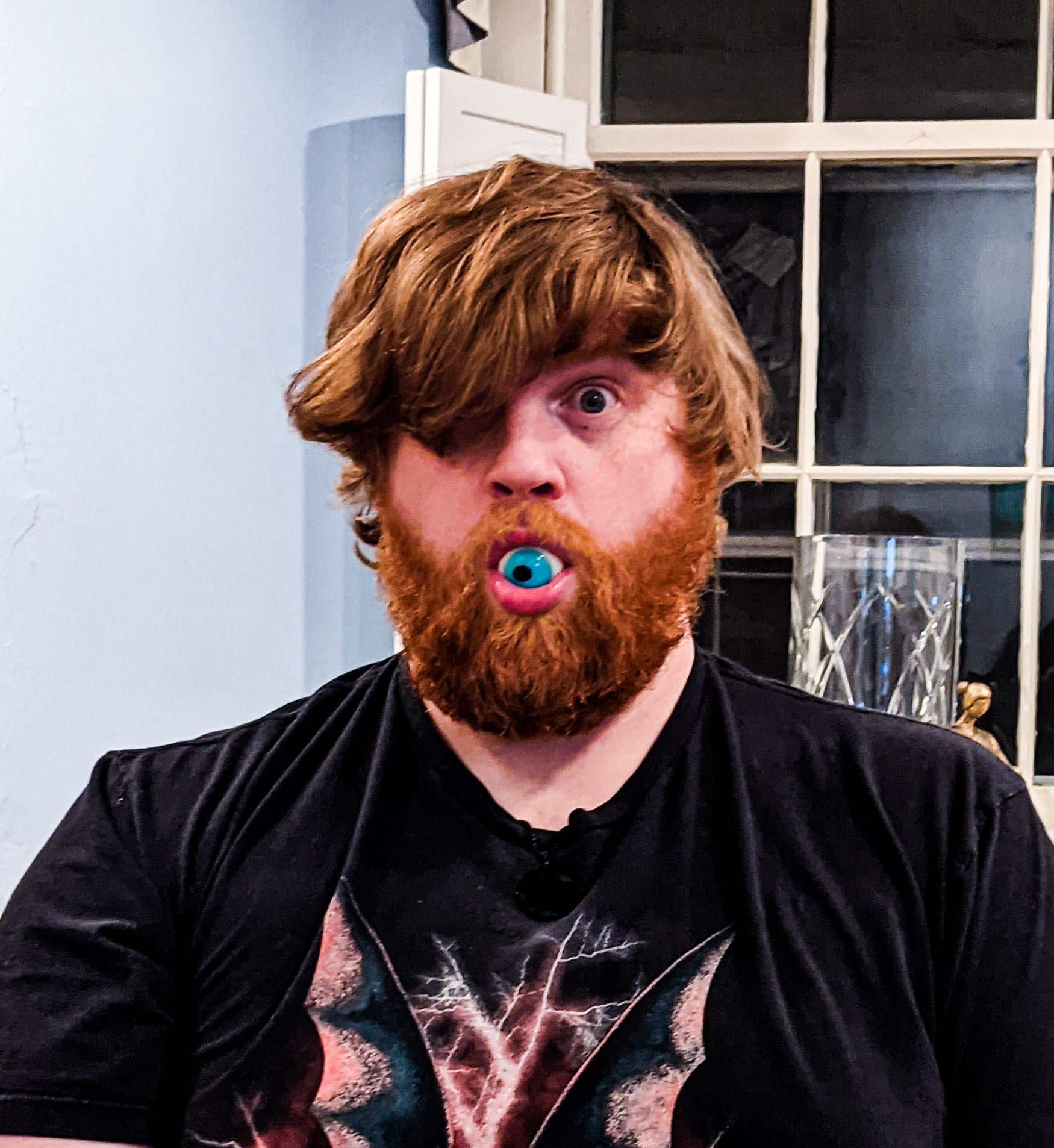 Image of a red-haired man with full beard and a novelty eyeball in his open mouth.