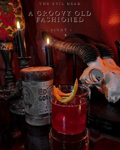 Dark image of a red cocktail lit by black candles with an animal skull in the background.