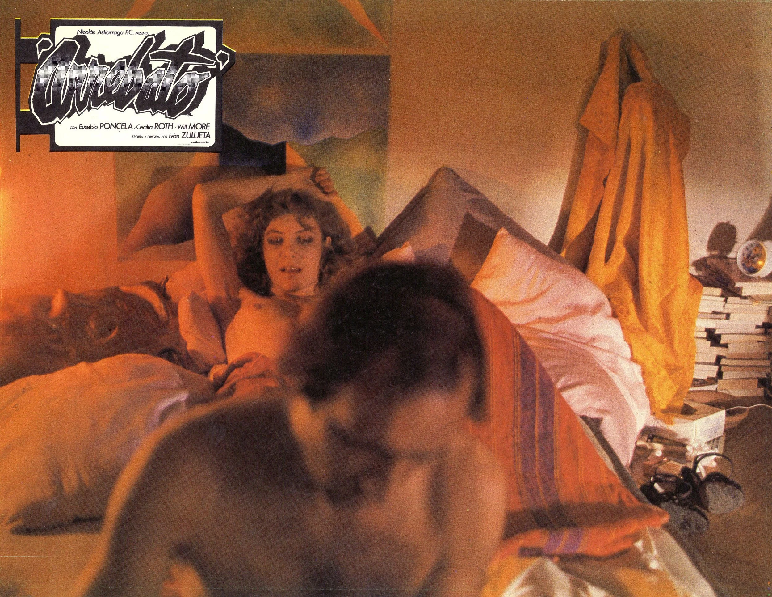 A woman lies naked on a bed while a man, also naked, sits on the edge of the bed facing away from her.