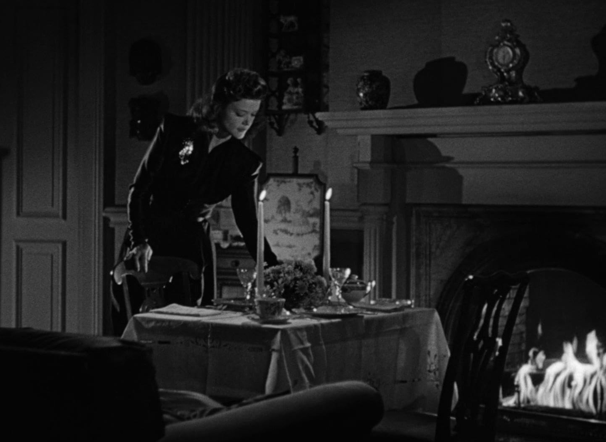 A woman sets a dinner table for two in front of a fireplace.