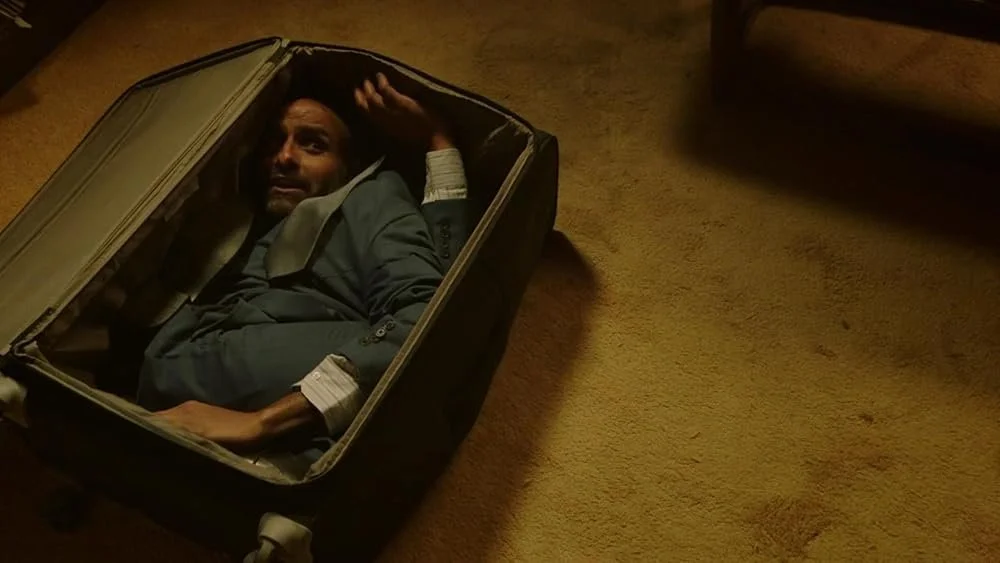 A man is stuffed into a suitcase, twisted beyond repair.