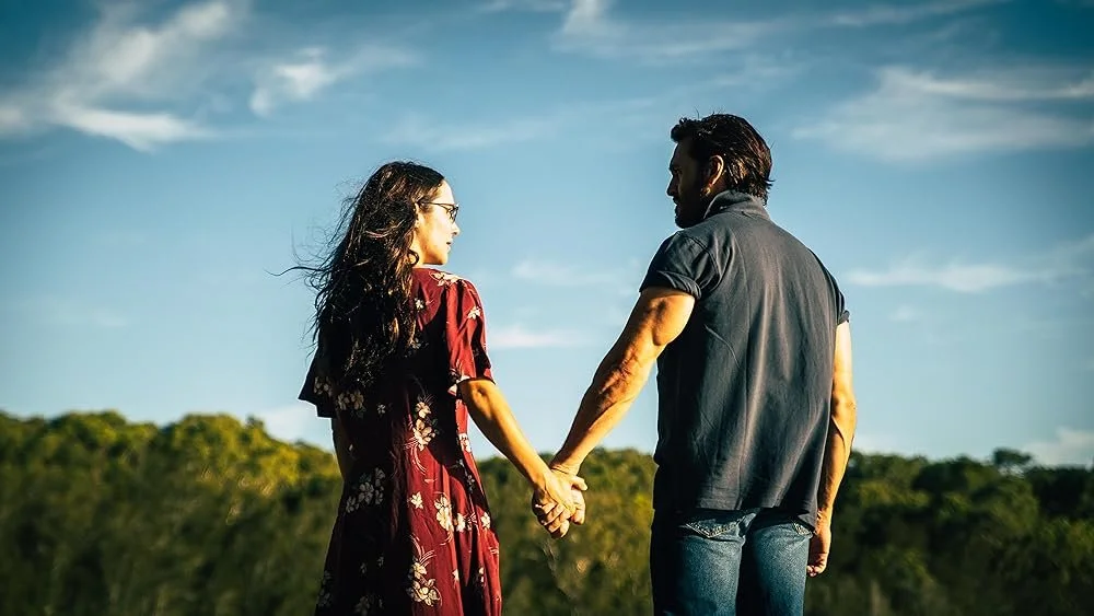 A man and woman stand hand in hand, facing away from the camera.