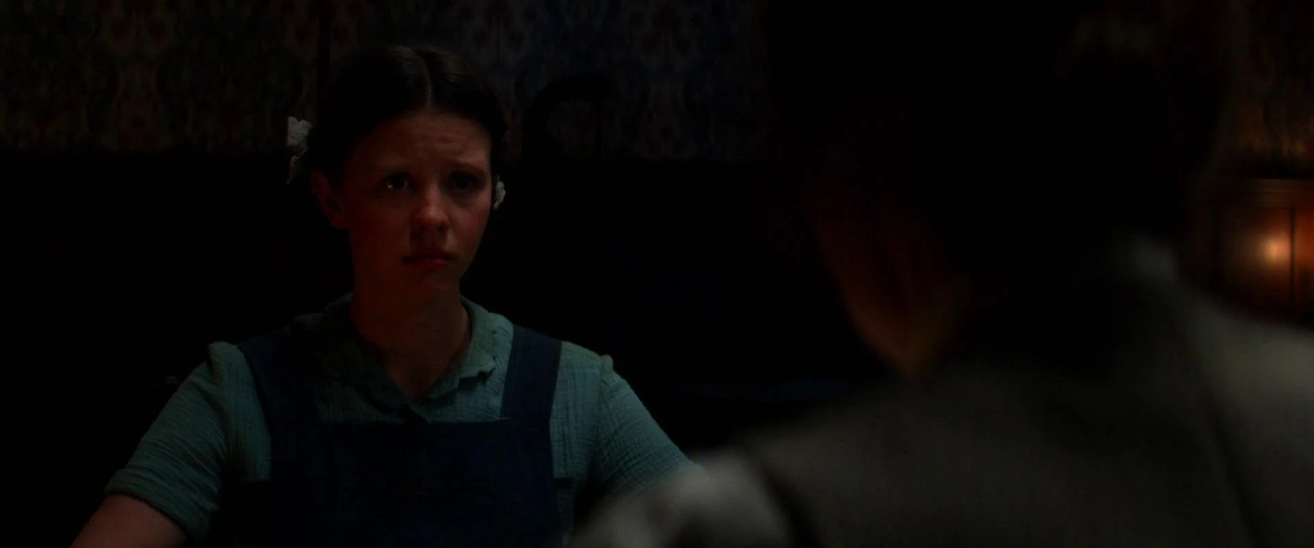 Pearl (Mia Goth) sits in darkness at the table with her mother.