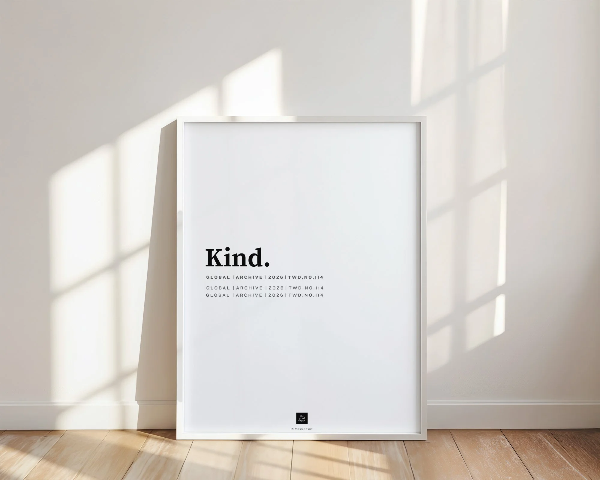 White poster with black text reading "Kind." inside a white frame, standing on a hardwood floor in front of a plain white wall with sunlight casting shadows through a window.