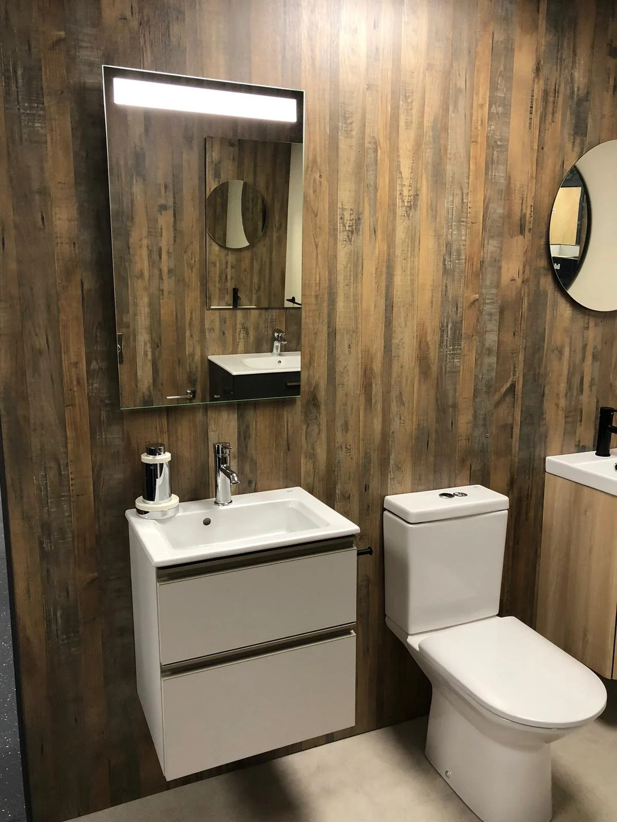 Bathroom with wood-paneled wall, white sink with black cabinet, toilet, and oval mirrors