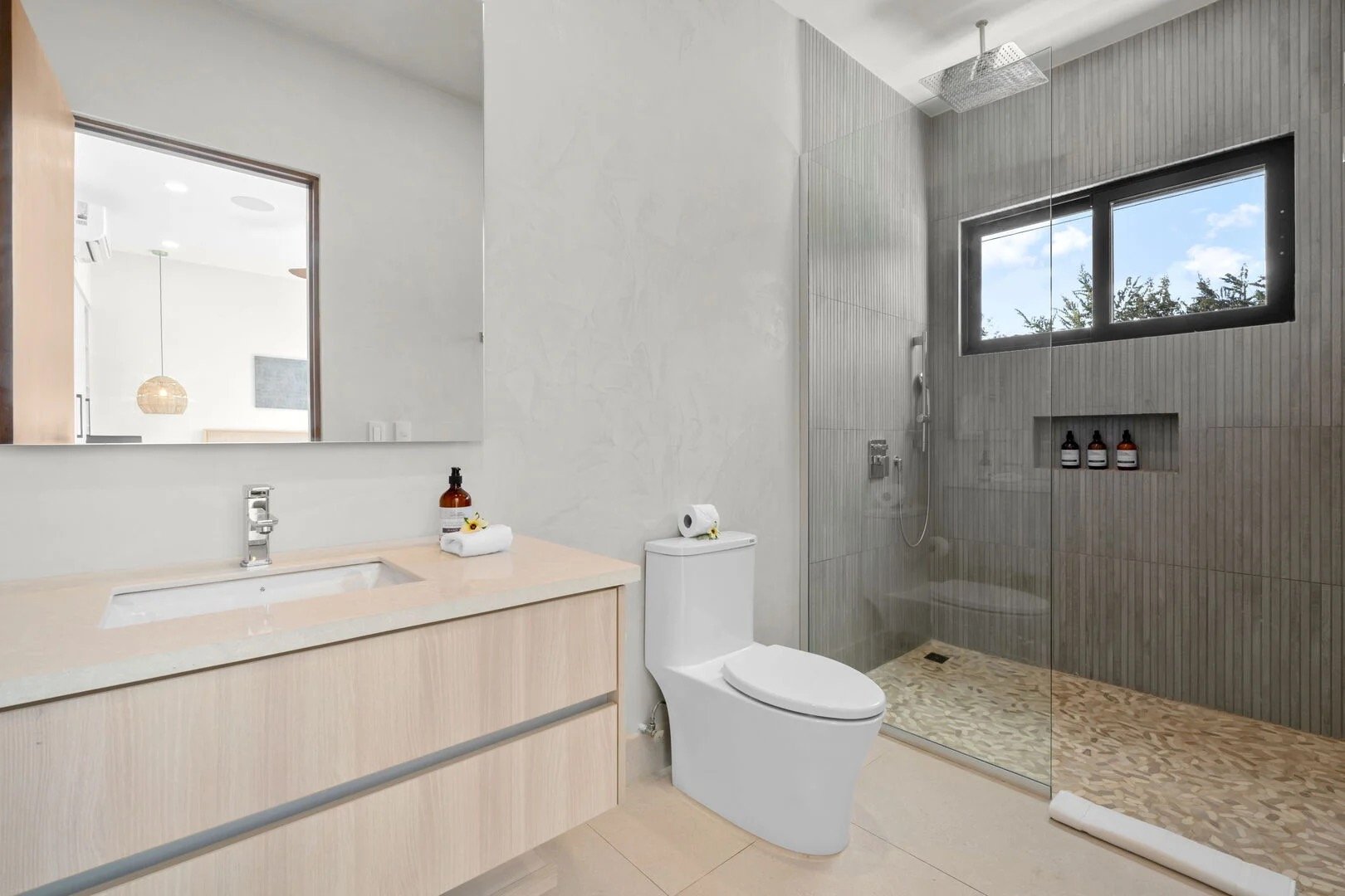 Modern bathroom featuring a large mirror, a vanity with a sink, a toilet with a paper roll, and a walk-in shower with a window and built-in shelves.