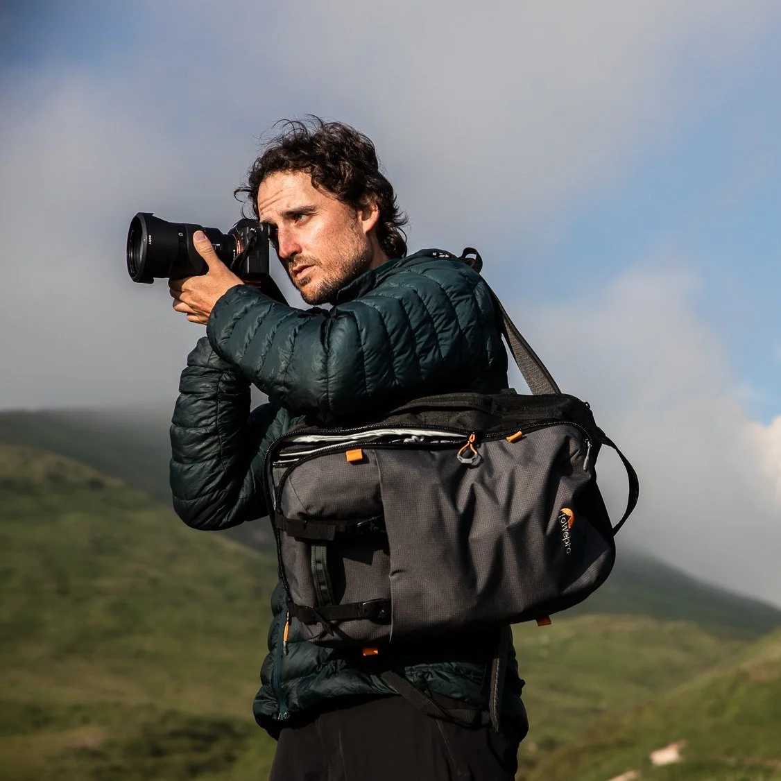 Chandler Borries, professional adventure photographer, holding a Sony camera and wearing a Lowepro camera bag in a mountainous landscape.