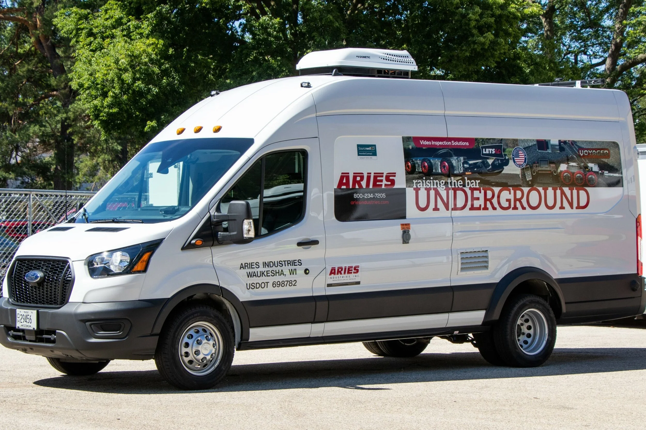White service van with Aries Industries branding and graphics, parked outdoors with trees in the background.