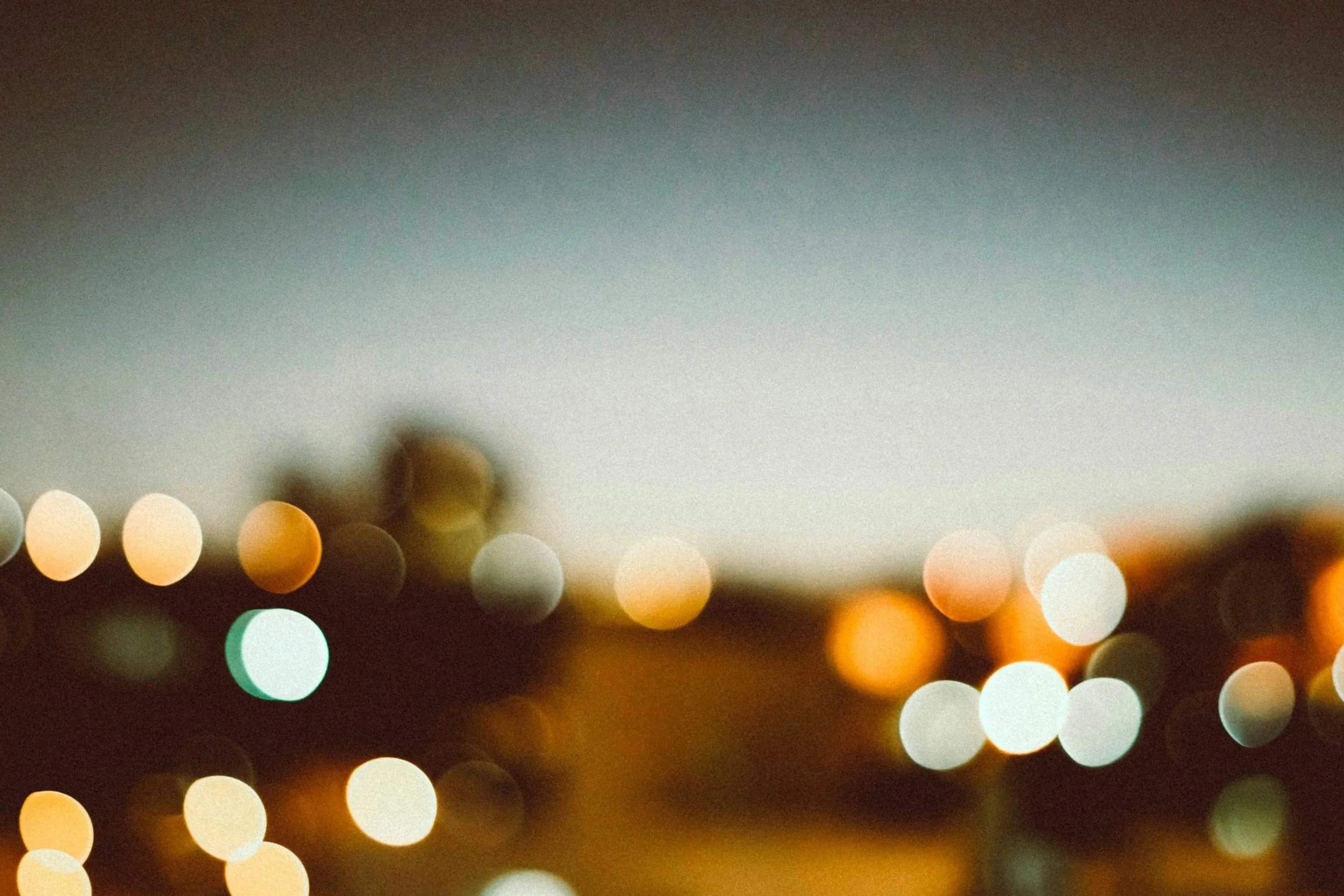 Blurred cityscape at dusk with bokeh lights and a faint gradient sky.
