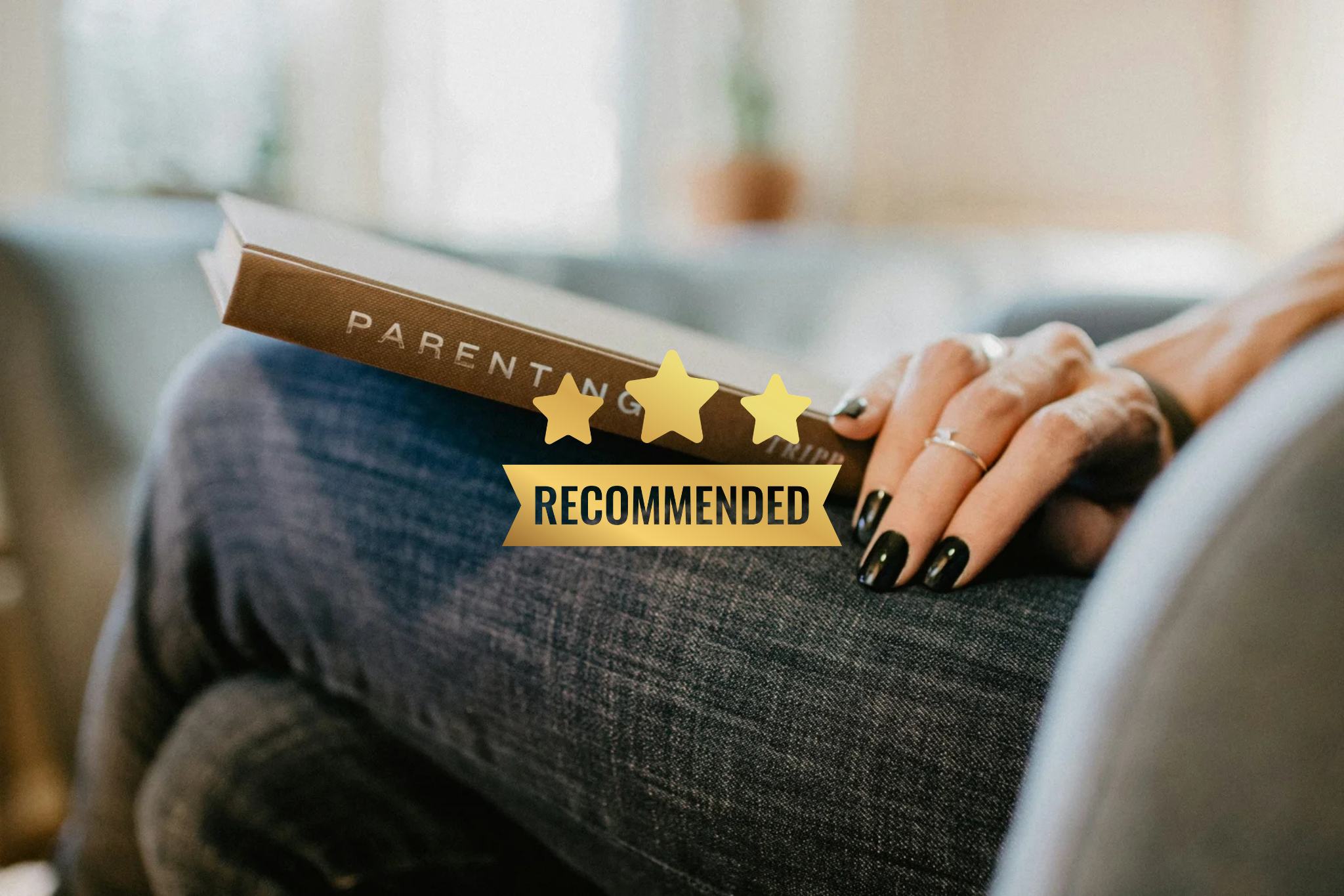 Close-up of a person holding a book titled 'Parenting' with a recommended rating overlay featuring three gold stars and a banner reading 'RECOMMENDED.' The person has dark painted nails and wears a ring on their finger. They are seated with denim fabric visible.
