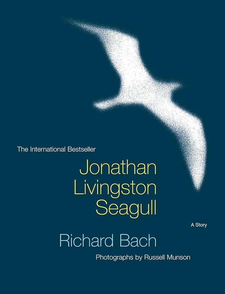Book cover of 'Seagull' by Jonathan Livingston Seagull, authored by Richard Bach, with photographs by Russell Munson, featuring a stylized white seagull in flight against a dark blue background.