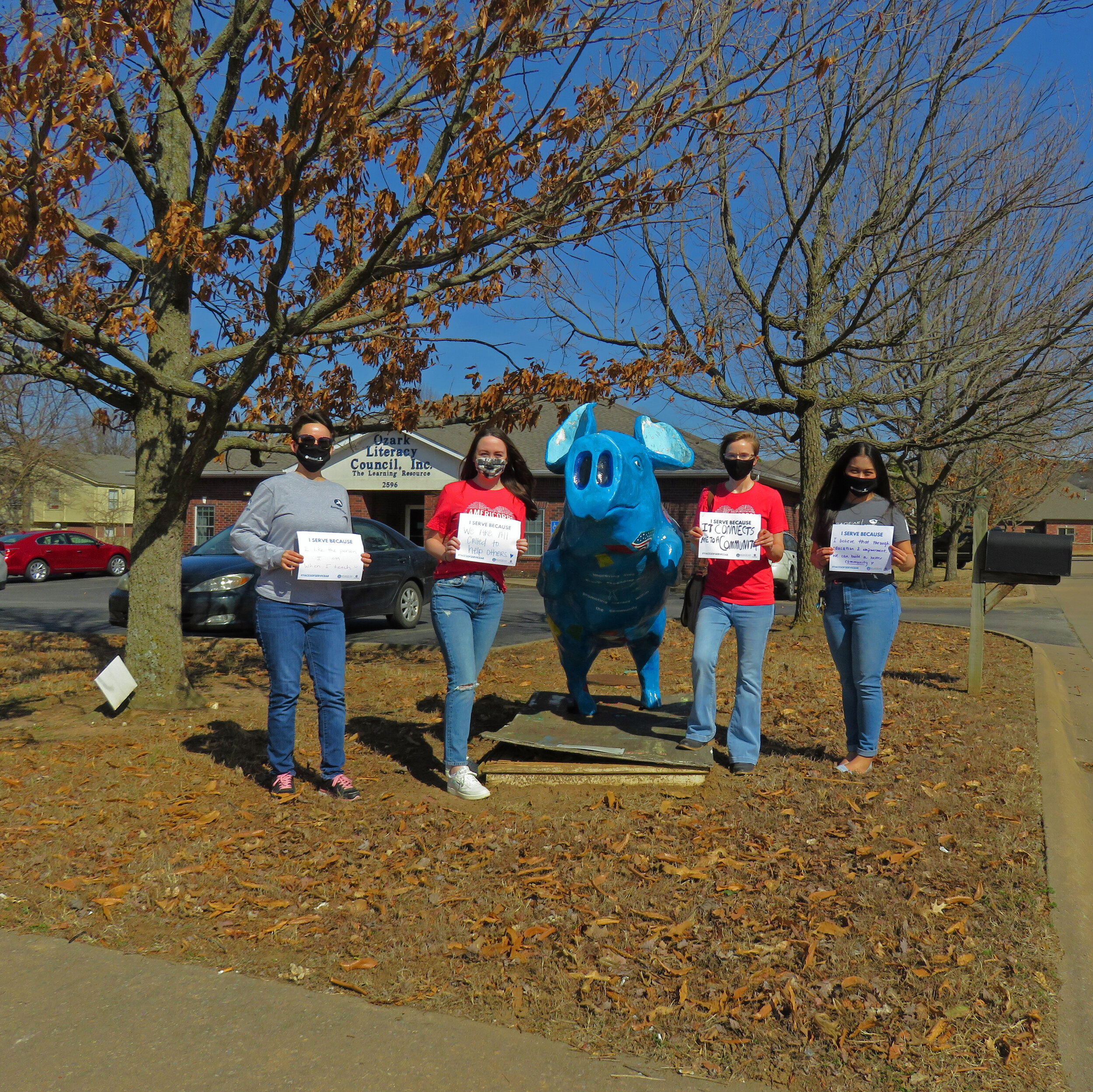 Four Americorps teachers stand by "Freedom" pig at OLC holding signs