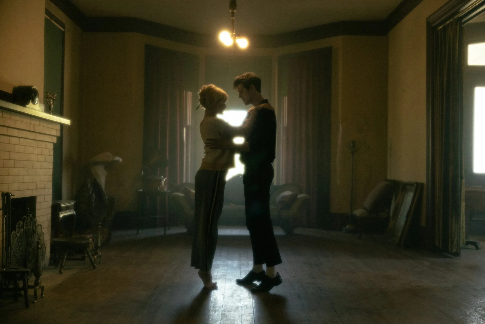 Silhouetted couple standing close and gazing at each other in a dimly lit room with sunlight streaming through curtains, illustrating the nuance of online sex therapy.