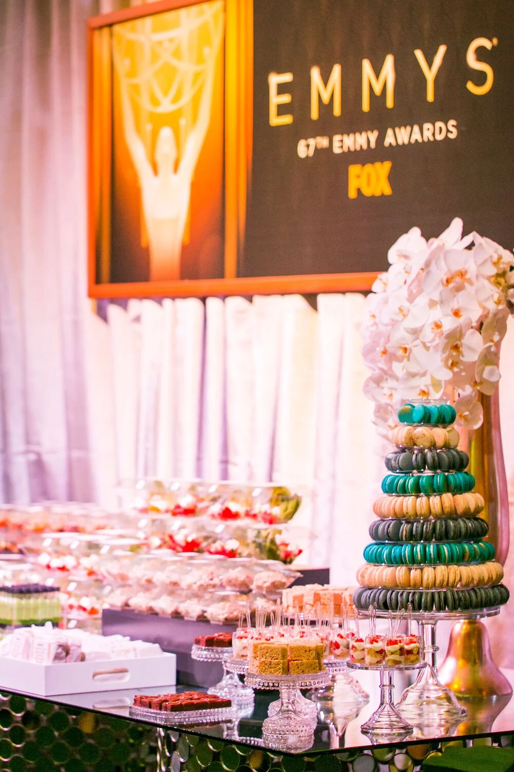 The Sixty Seventh Emmy Awards tablescape displaying a mixed, bite sized desserts and a colorful macaron stand sitting on a glass table