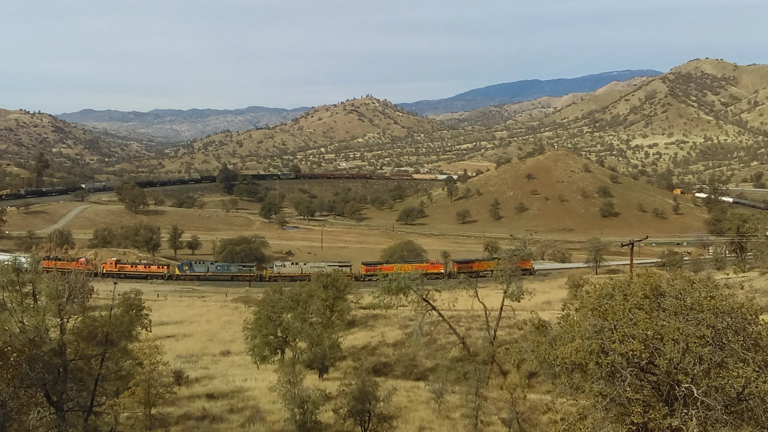 Built in 1876, the Tehachapi Pass Line was the first railroad into Southern California. To keep the incline to a steady 2.2% grade, the line makes multiple sweeping curves and crosses over itself hallway up the grade to Tehachapi, in Walong, CA. In this photo, a BNSF manifest freight navigates the loop, crossing over itself in the process. Photo by Alex Lewis, 2018.