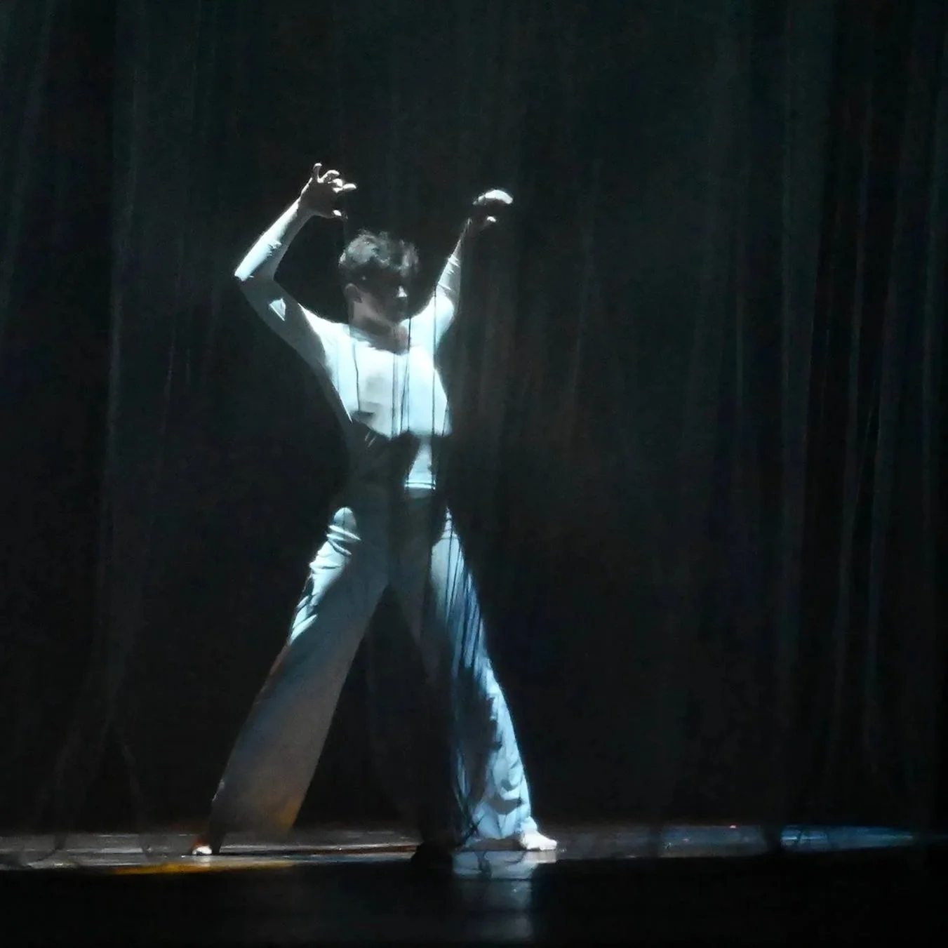 A solo male dancer on stage highlighted in dramatic spotlight.