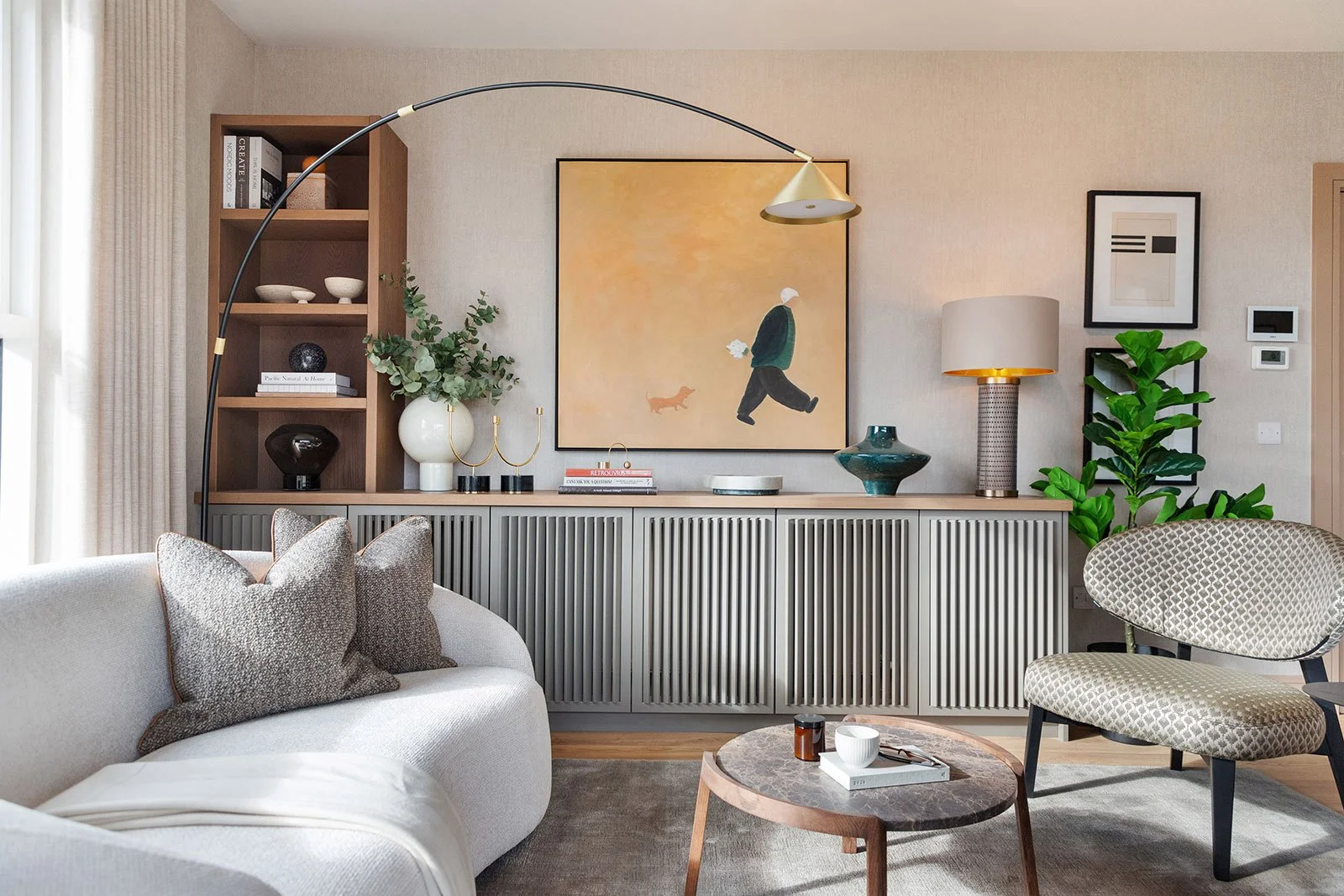 Seating area with curved couch, round coffee table, large chair and painting in the background