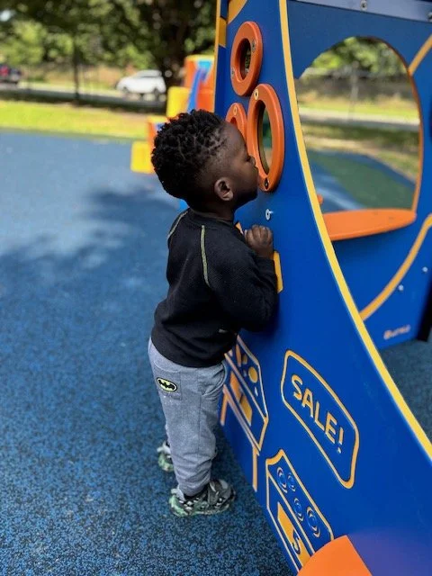 Young child interacting with a blue and orange play structure at a playground.