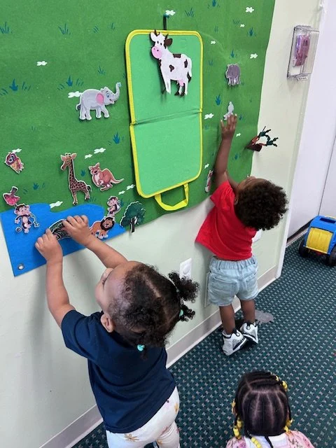 Two young children playing with animal-themed felt boards and stickers on a classroom wall.