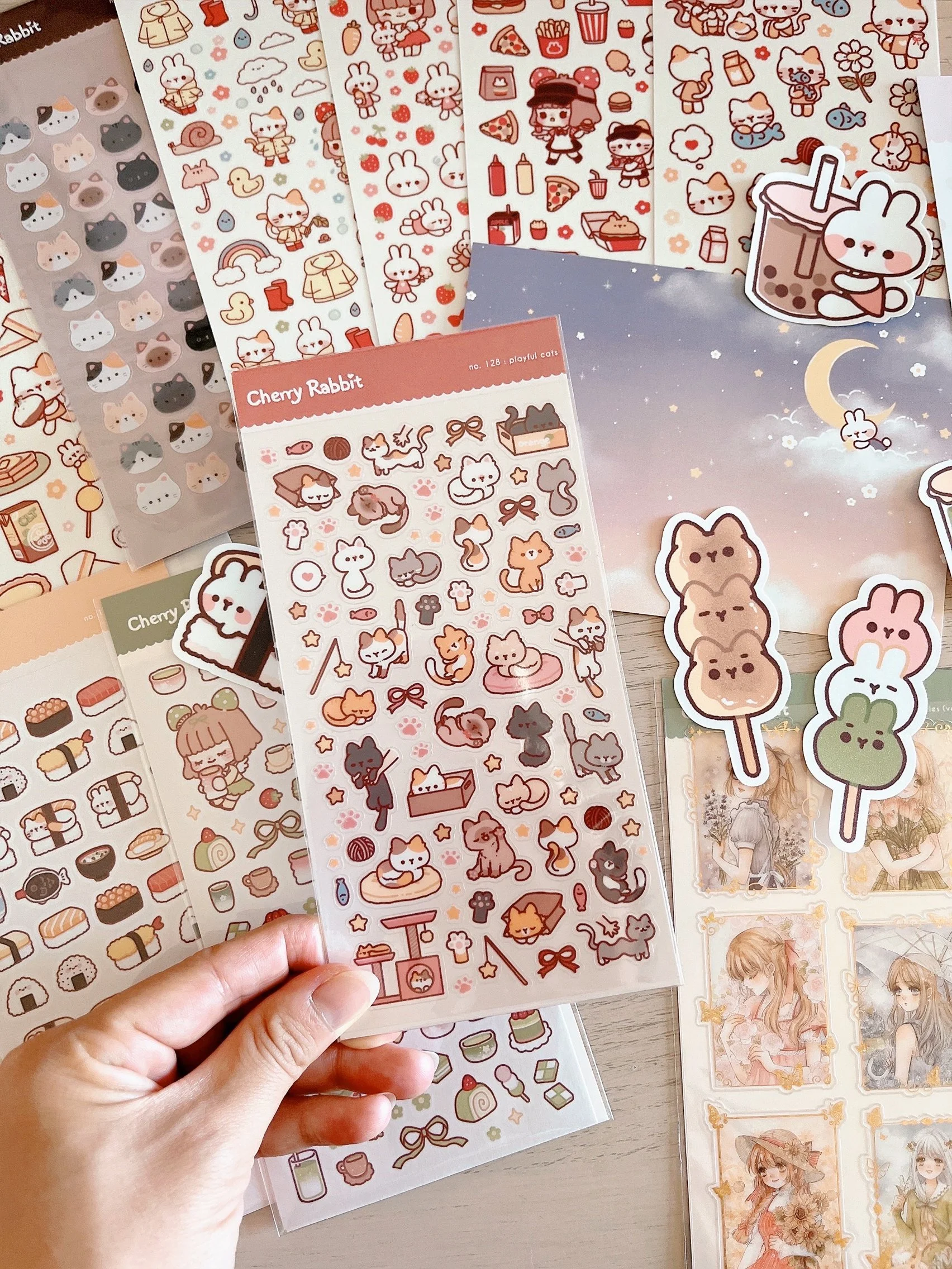 Collection of cute stickers featuring cats, bunnies, and food items, with some stickers attached to paper or bubble tea cups.