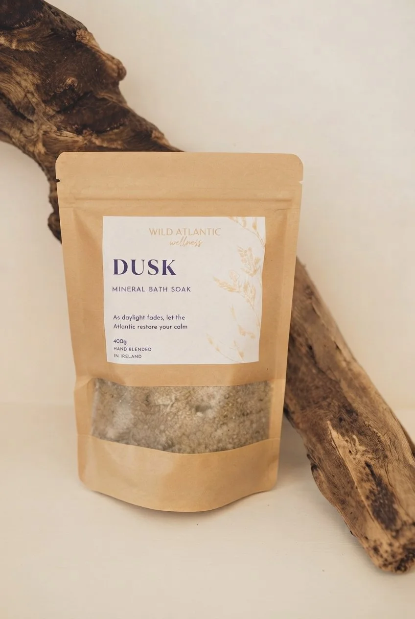 Wild Atlantic Wellness Dusk mineral bath soak in a kraft pouch beside Atlantic driftwood