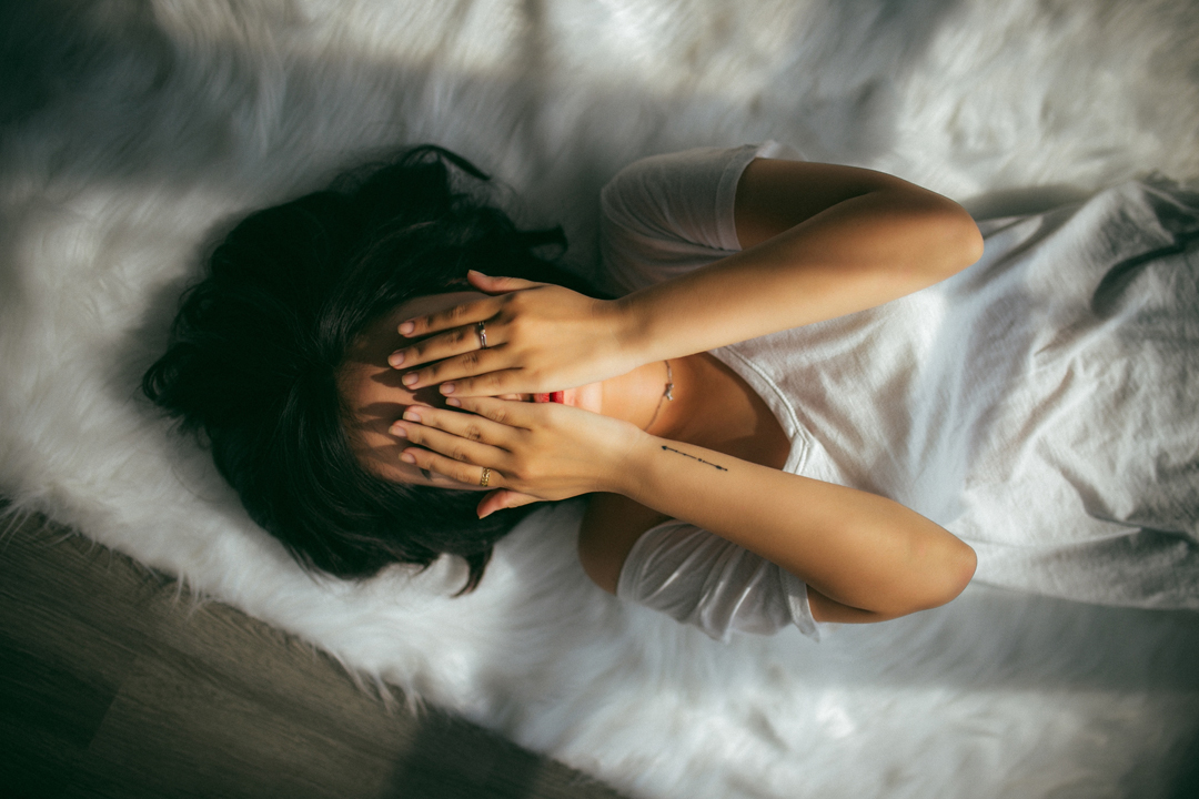 Woman who is stressed out lays on the floor covering her eyes.
