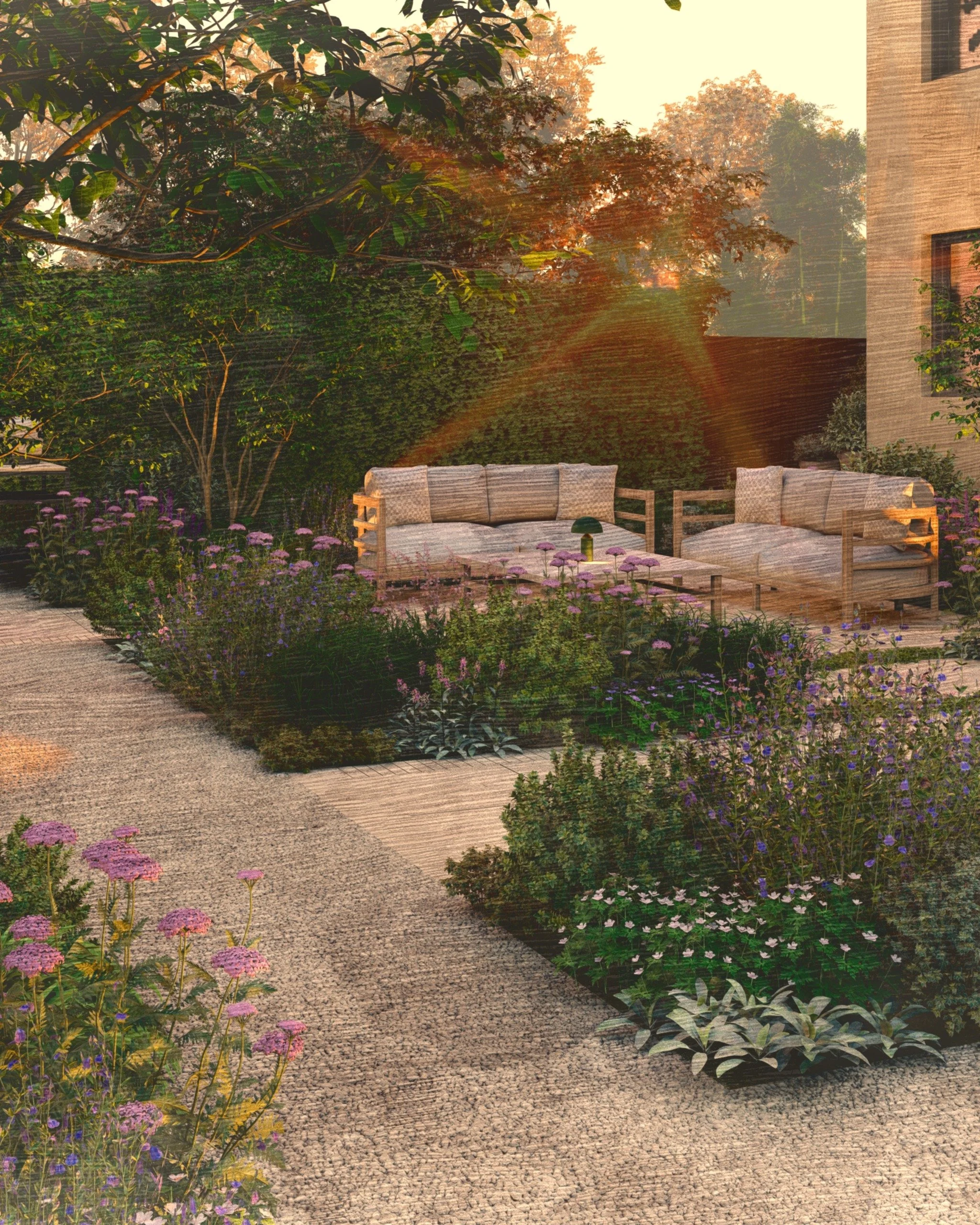 Two wooden outdoor sofas with cushions are placed on a gravel pathway in a lush garden with colorful flowers, trees, and a building in the background at sunset.