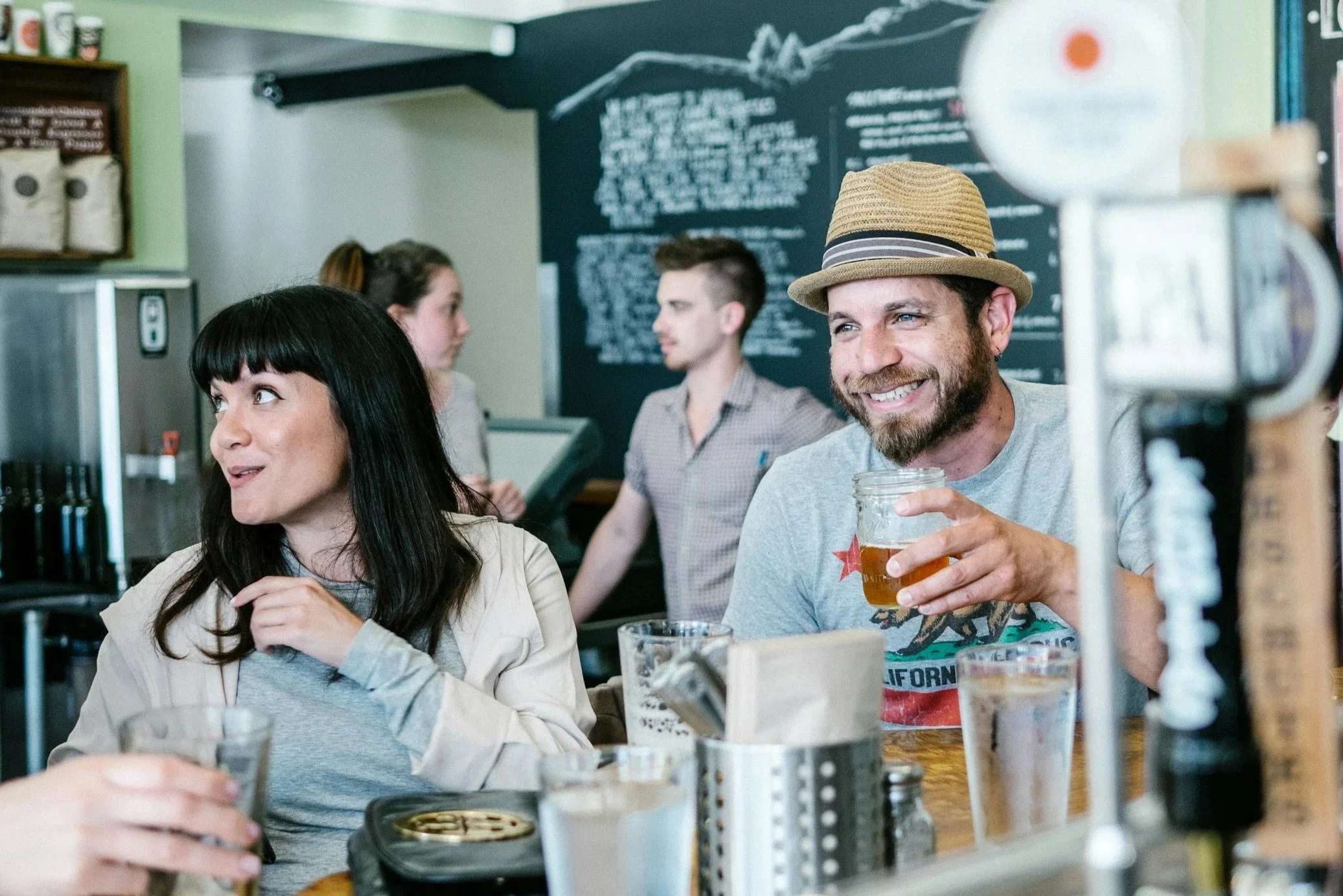a woman with dark hair and a man wearing a fedora with expressive smiles sitting at a craft brewery in Richmond VA.jpg