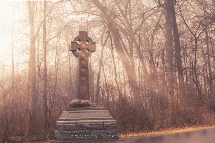 A Celtic-cross memorial stands in a sunlit grove of bare trees at Gettysburg.