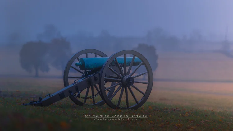 A lone cannon stands in a misty Gettysburg field in cool blue light.