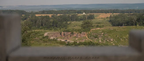 View from the 12th and 44th New York Infantry Monument on Little Round Top looking down toward Devil’s Den, framed by foreground stonework.