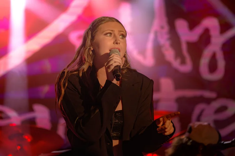 A singer holds a microphone beneath pink and red stage lighting.