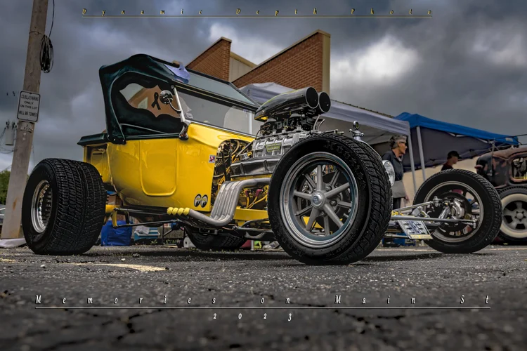 A yellow hot rod is photographed from a low angle beneath dark clouds.