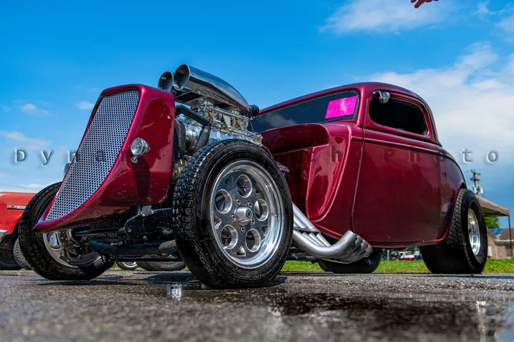 A burgundy hot rod is photographed from a low angle at an outdoor car show.