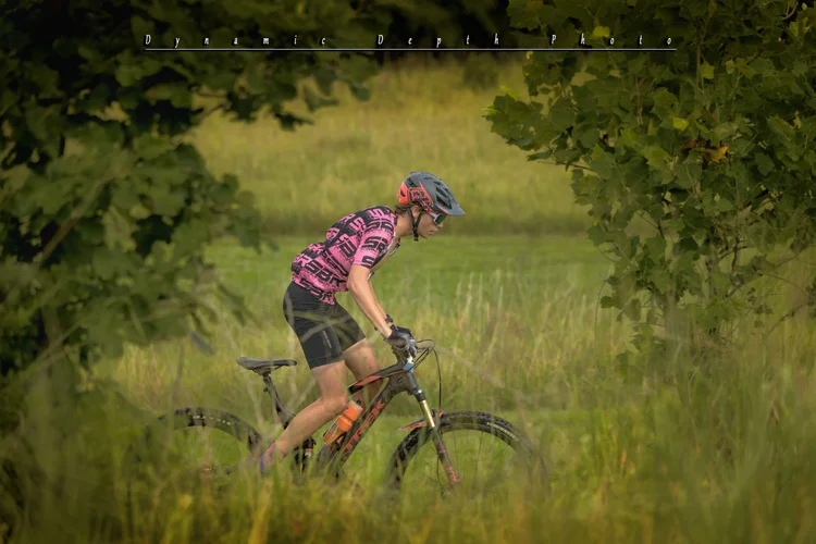 A cyclist rides through tall grass beneath overhanging leaves.