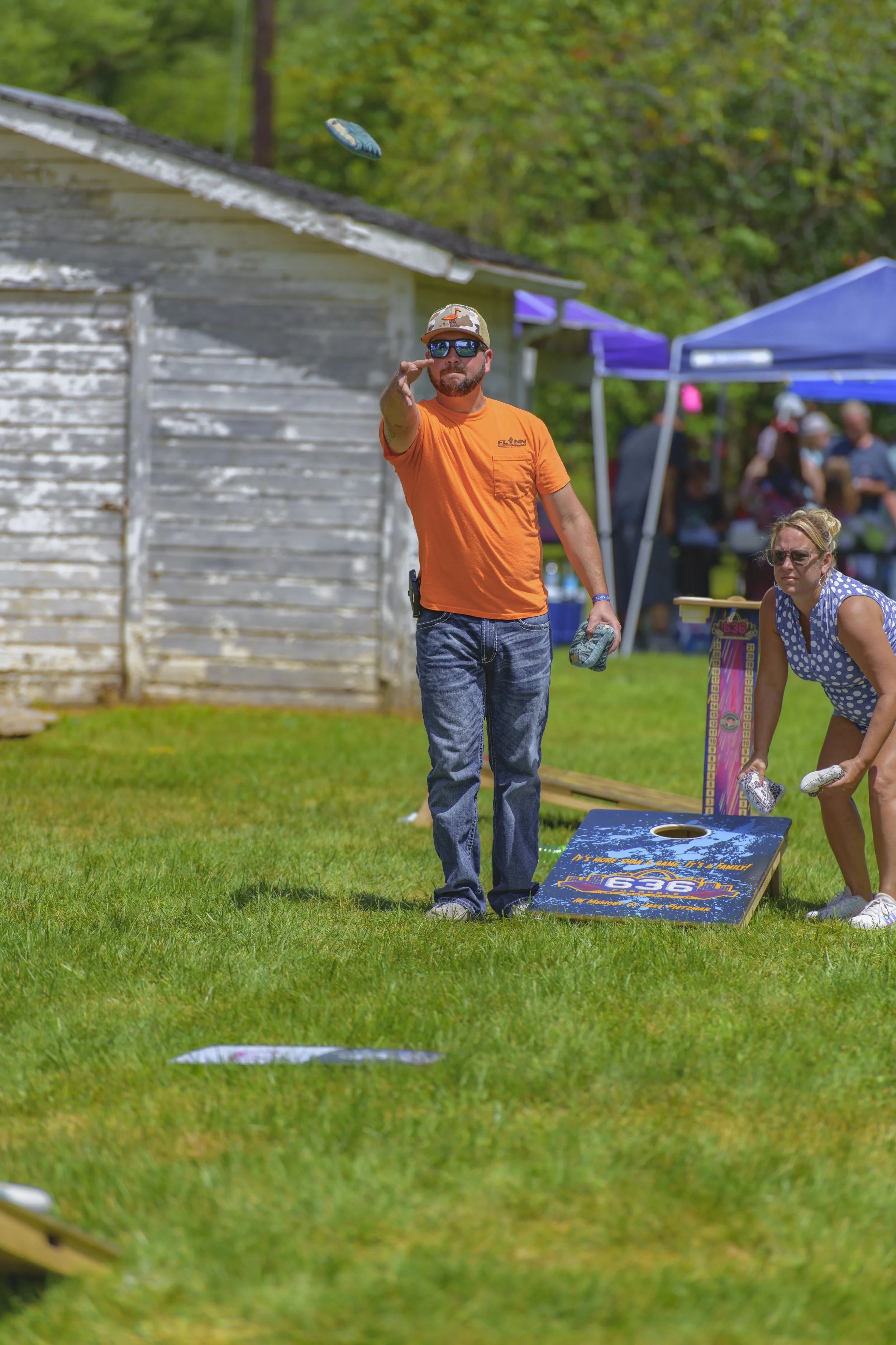 A player in an orange shirt tosses a beanbag across the grass at the 2022 Silex Festival.
