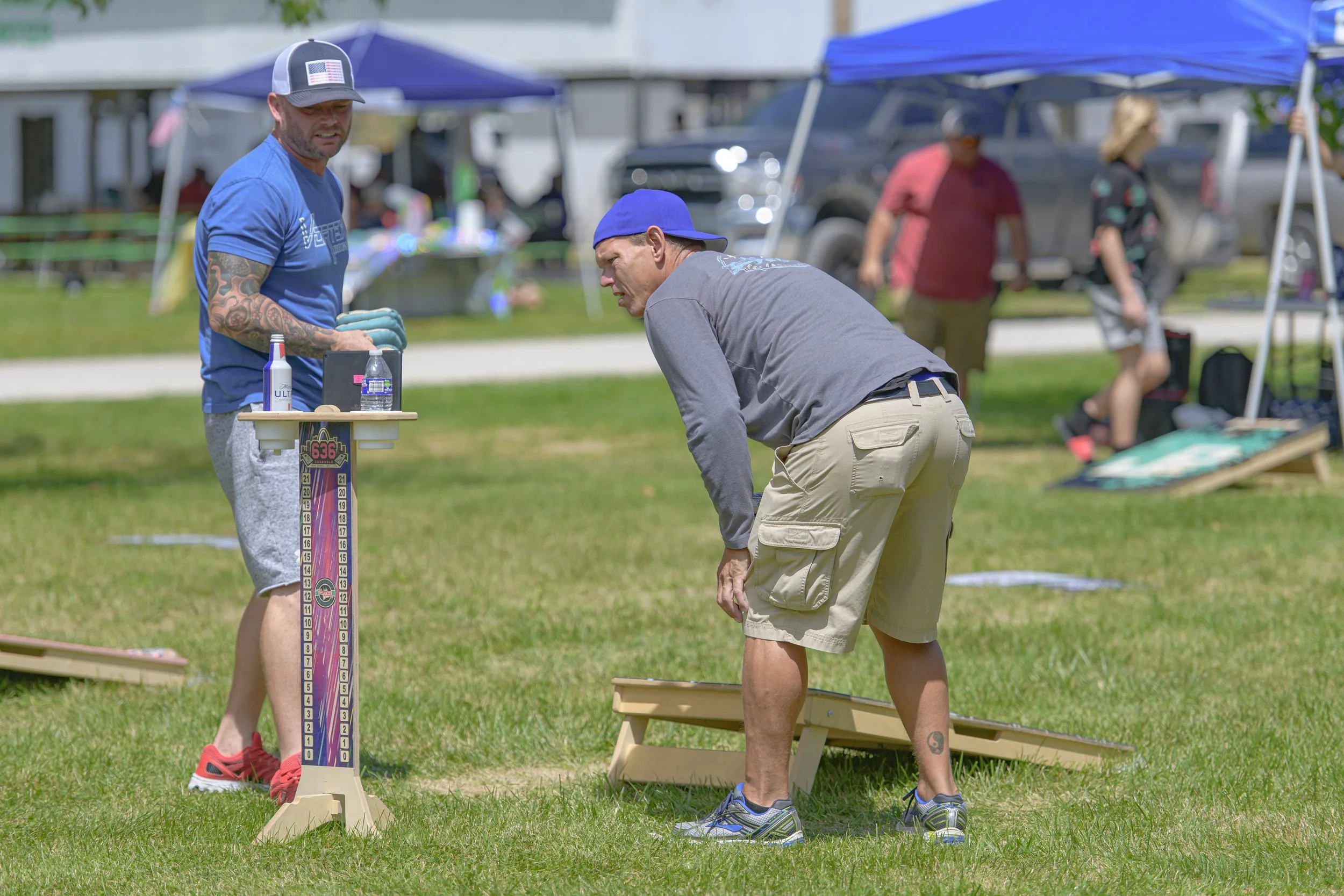 Two players wait beside a cornhole board, one leaning forward at the 2022 Silex Festival.