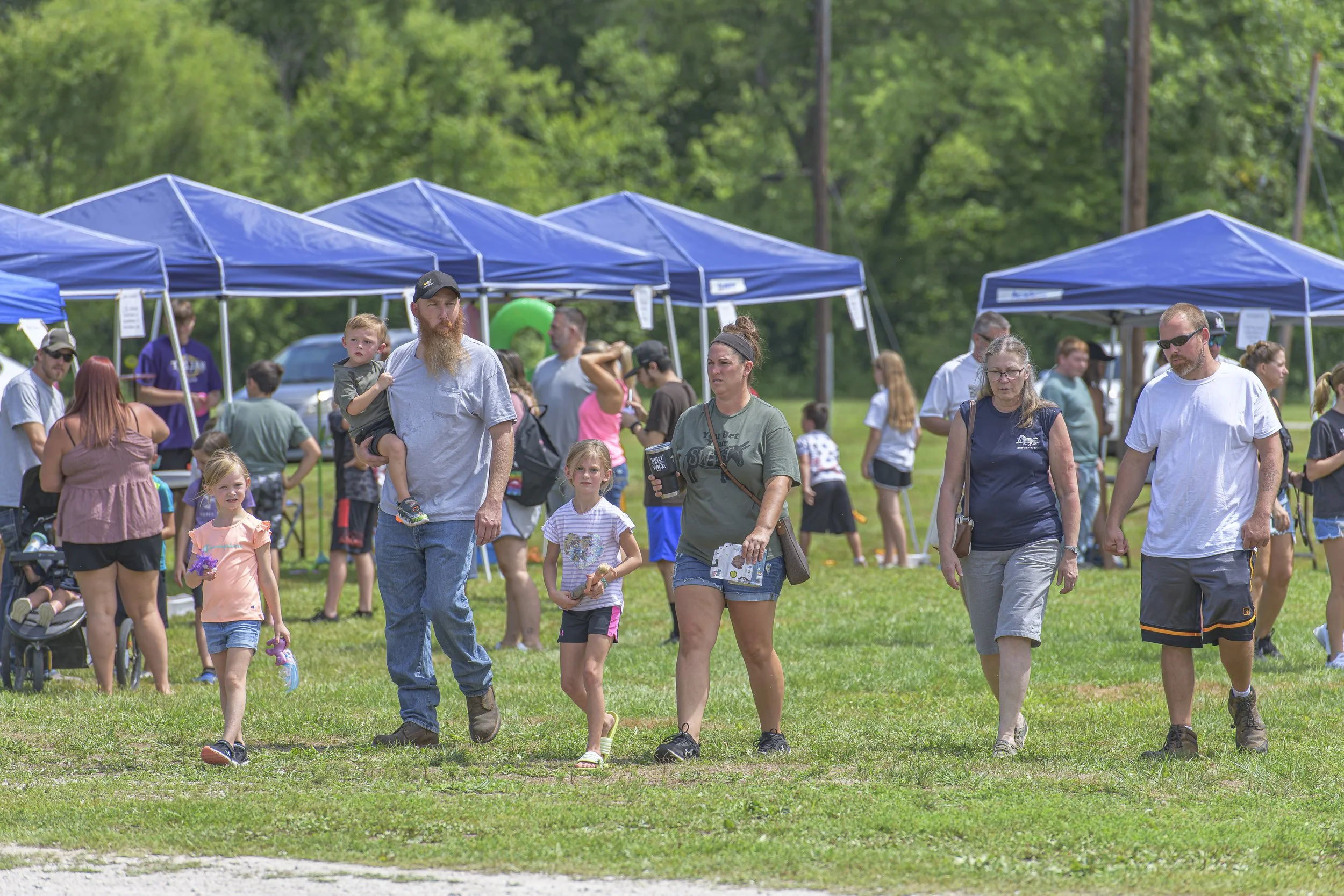 Visitors walk across the grass away from the rows of blue canopies at the 2022 Silex Festival.