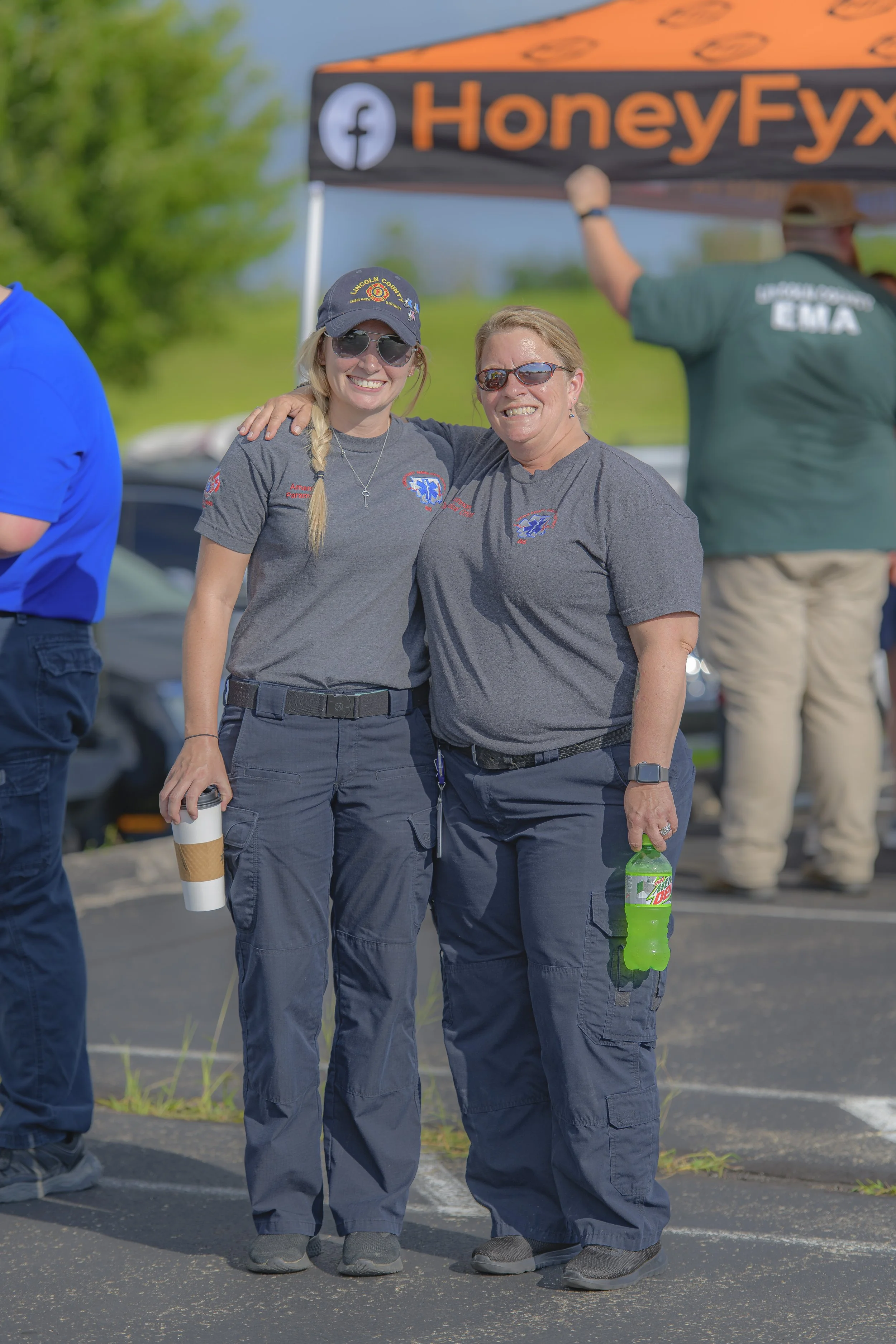 Two attendees in matching gray shirts pose together near an event canopy at the 2022 National Night Out.