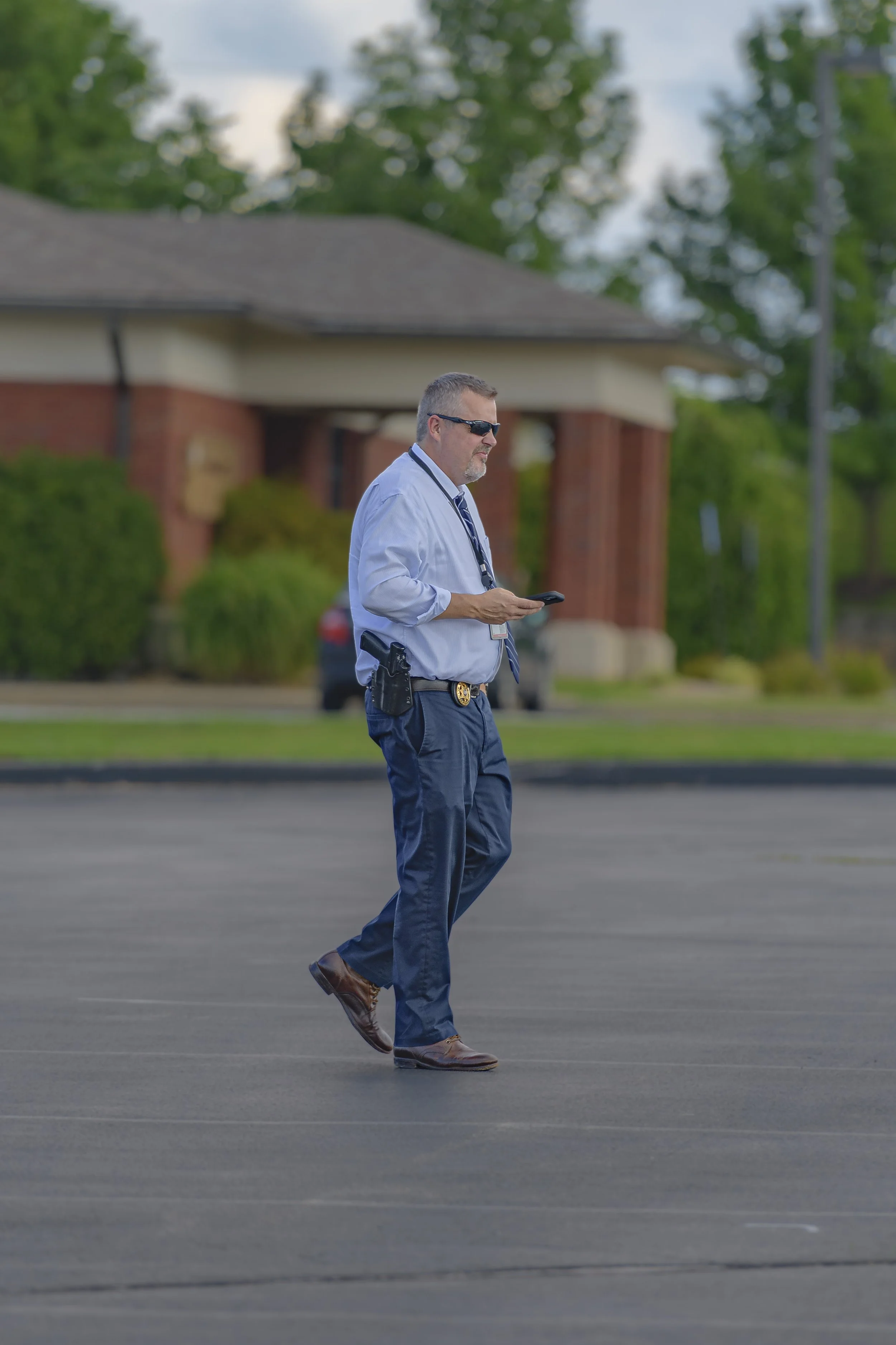A uniformed officer walks across the parking lot while holding a phone at the 2022 National Night Out.