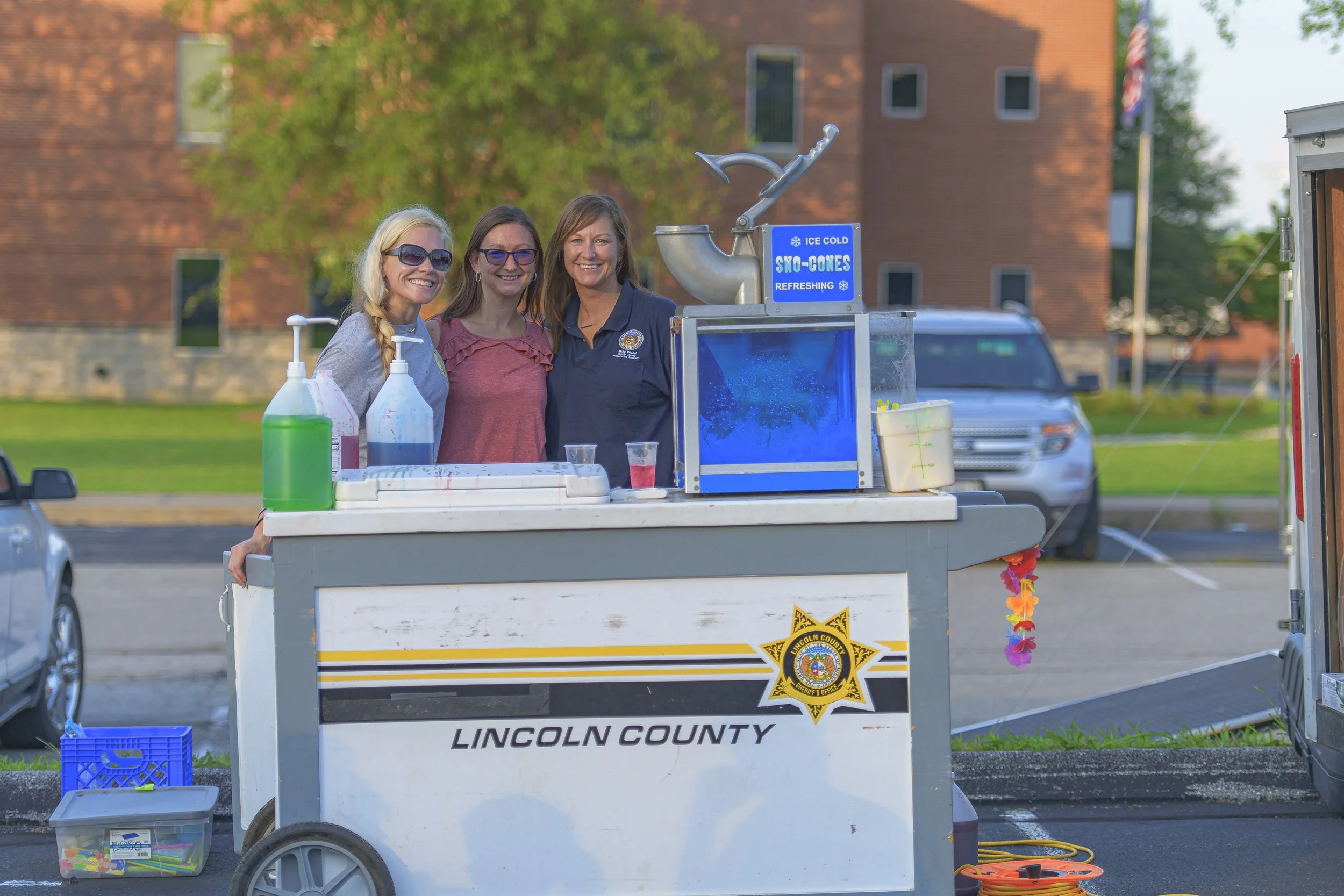 Three attendees pose behind a refreshment cart marked Lincoln County at the 2022 National Night Out.