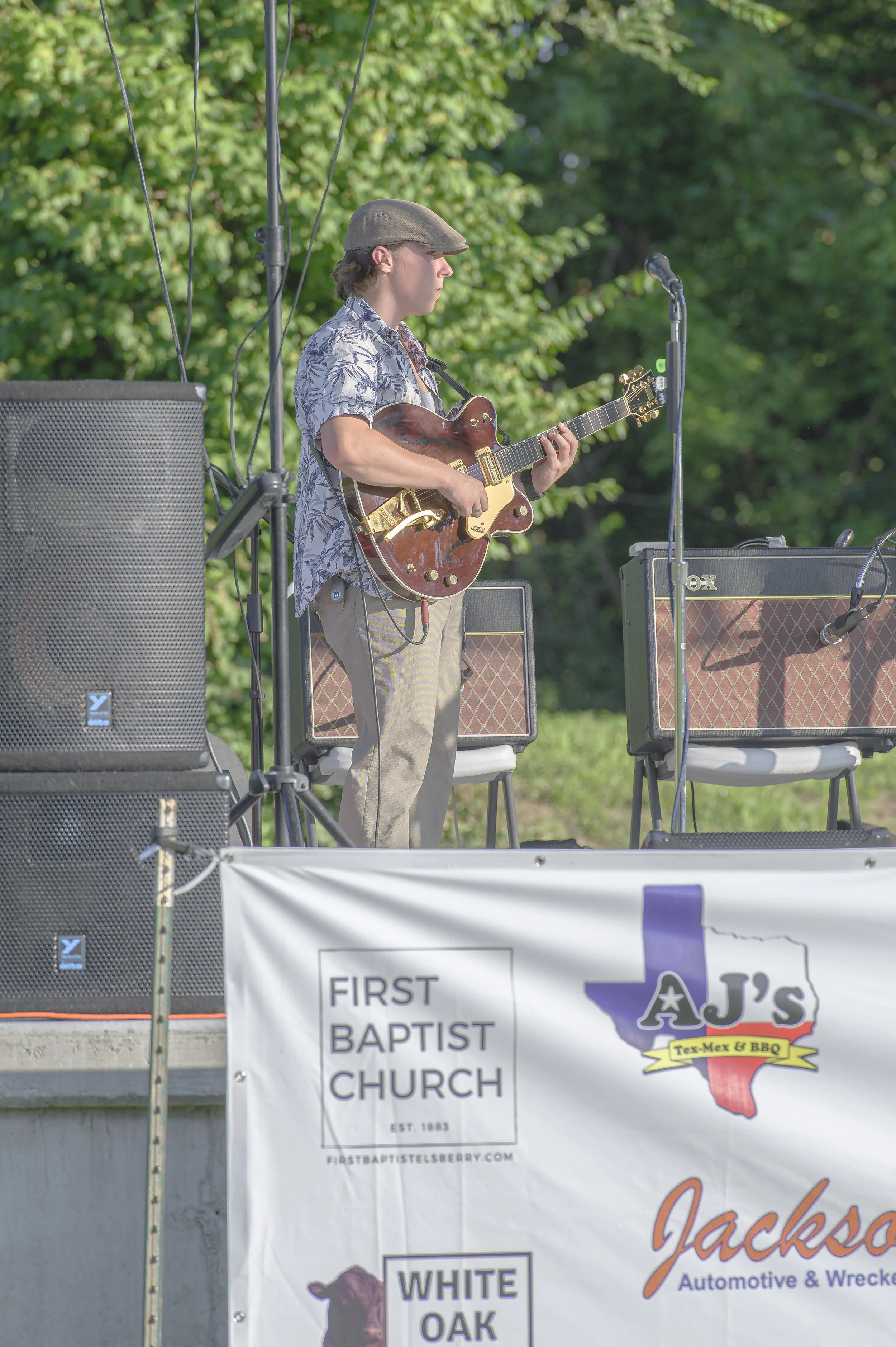 A guitarist in a flat cap plays a hollow-body electric guitar beside stage speakers at the 2022 ECGA Concert.