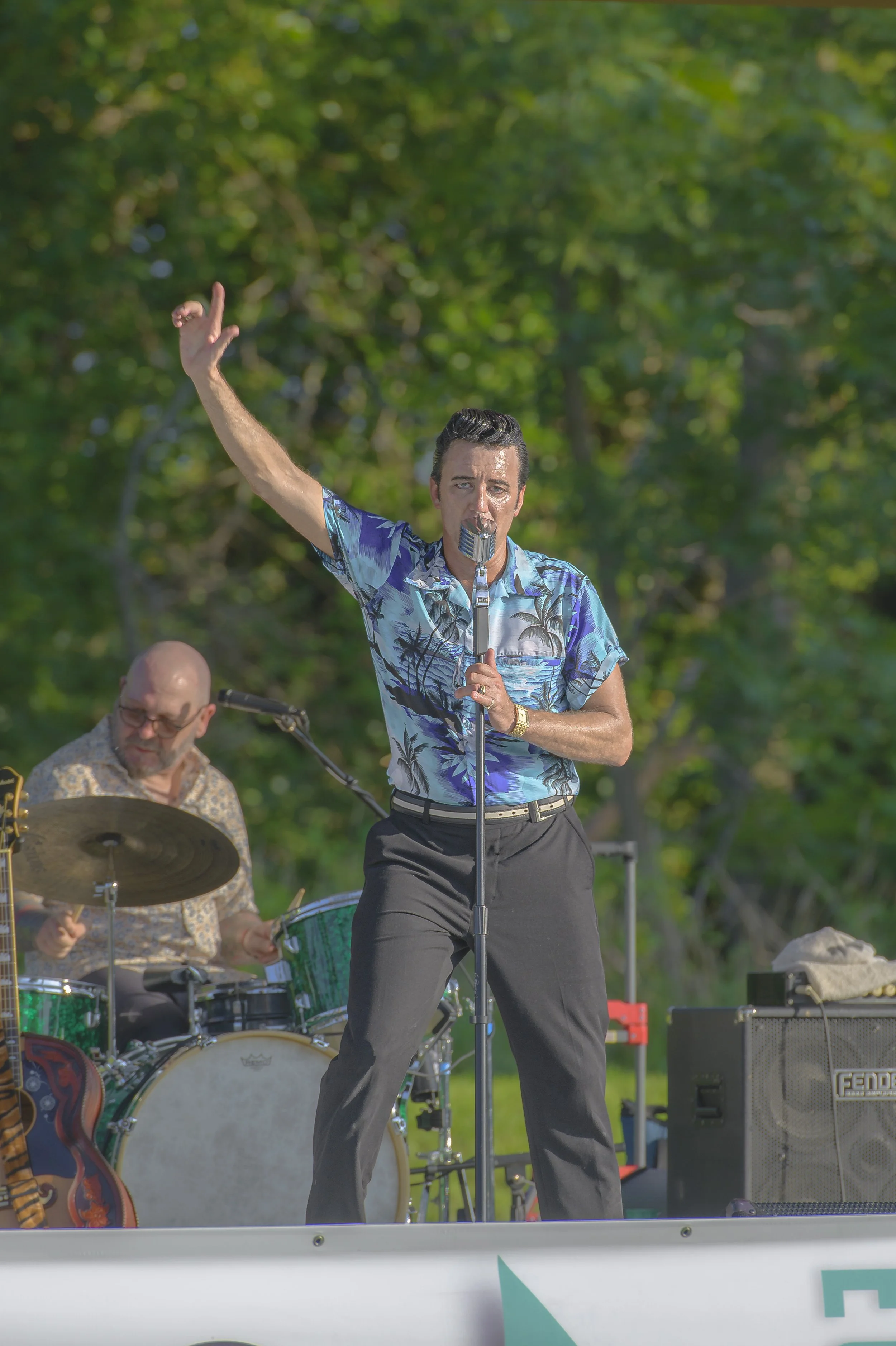 A singer in a blue patterned shirt raises one arm beside a microphone, with a drummer behind him at the 2022 ECGA Concert.