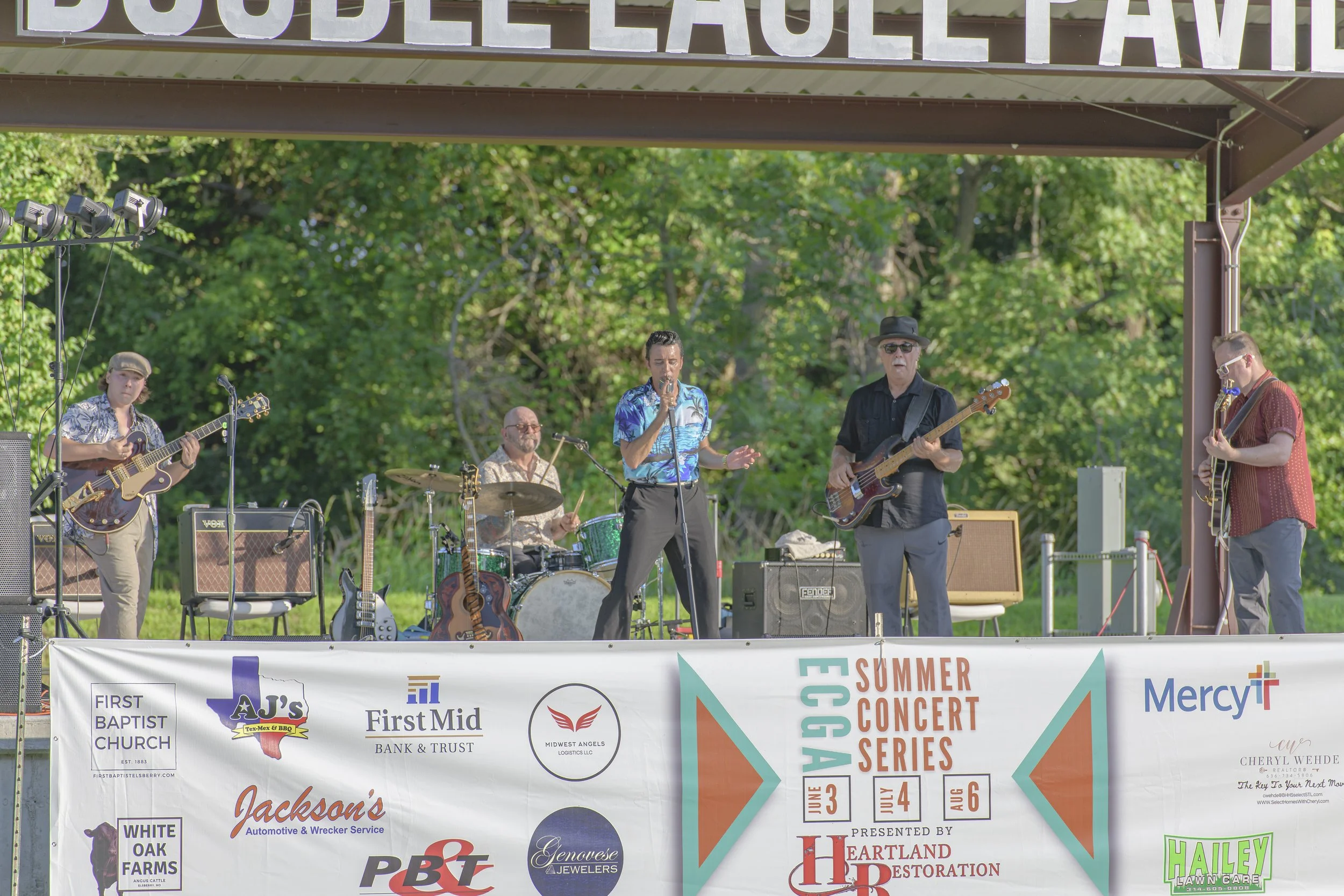 Musicians perform together on the outdoor pavilion stage at the 2022 ECGA Concert, with a summer concert banner along the front.