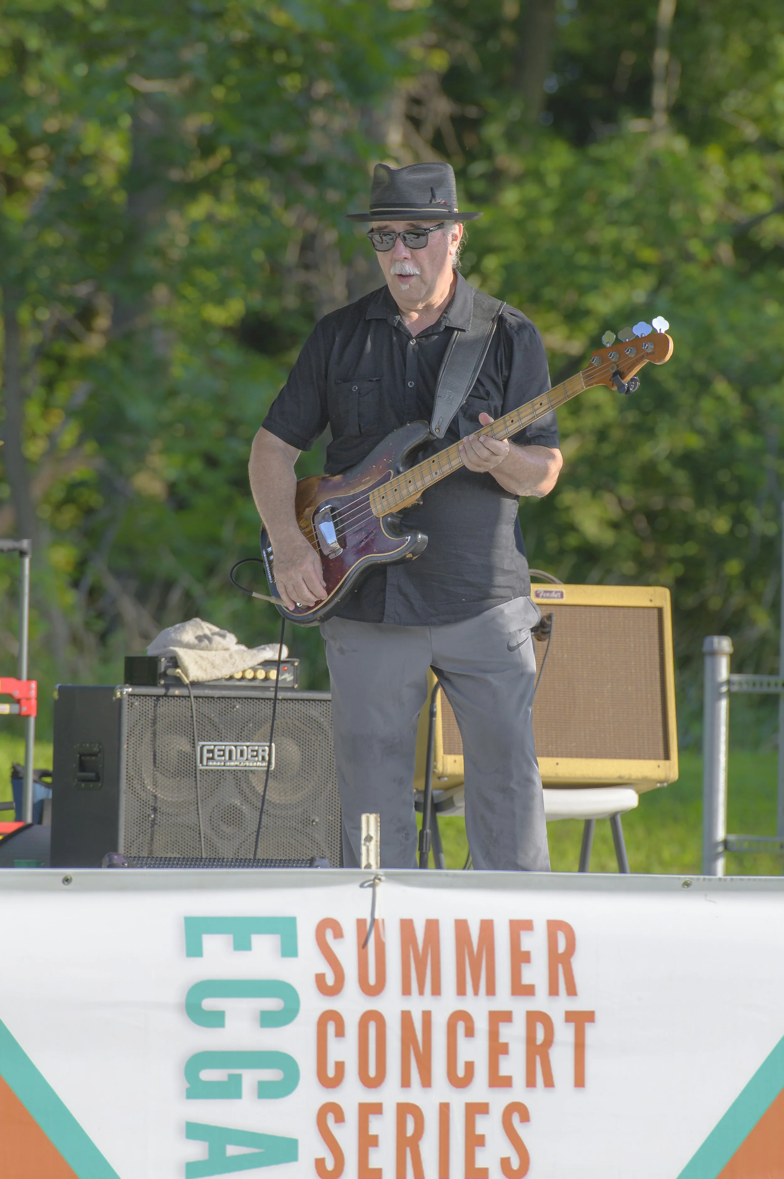 A bass guitarist wearing a dark hat and sunglasses performs on the outdoor stage at the 2022 ECGA Concert.